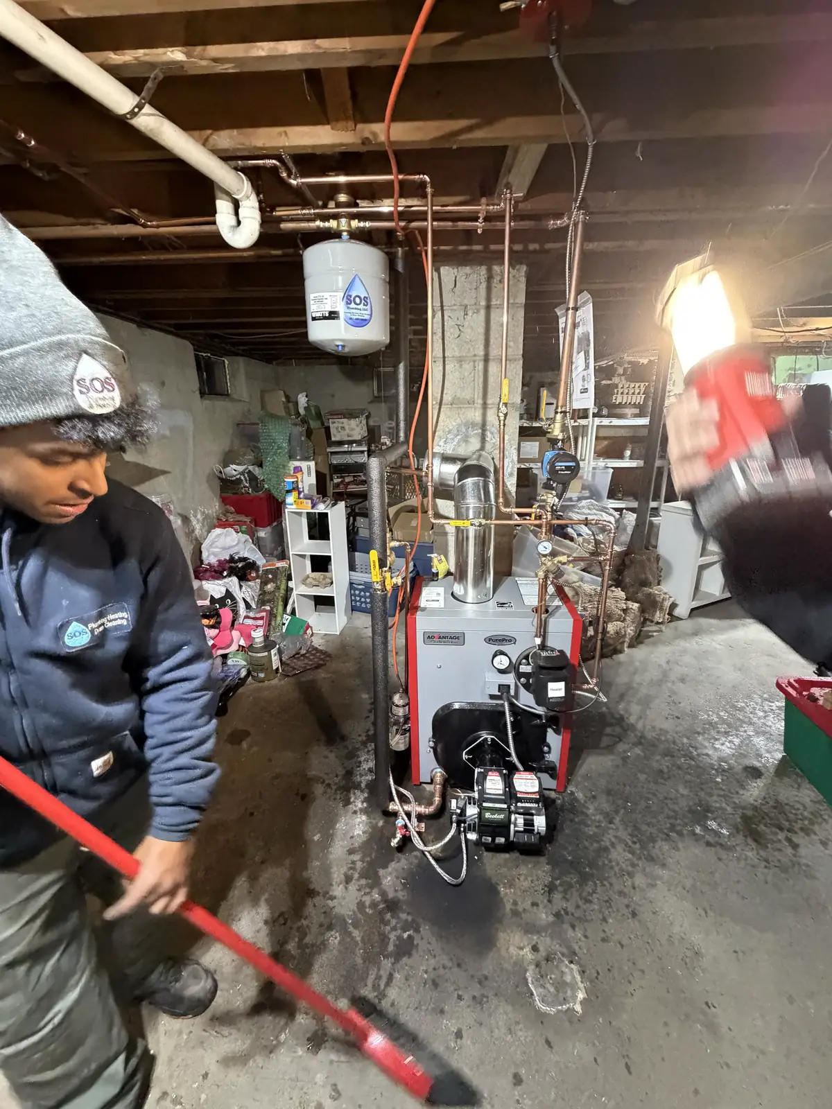 SOS technician sweeping up after completing a boiler installation in a Rhode Island basement