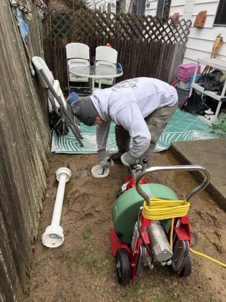 SOS technician running a drain machine at an outdoor cleanout in Rhode Island