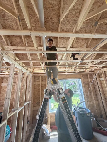 SOS plumber running rough-in piping through floor joists on a Rhode Island new-construction site