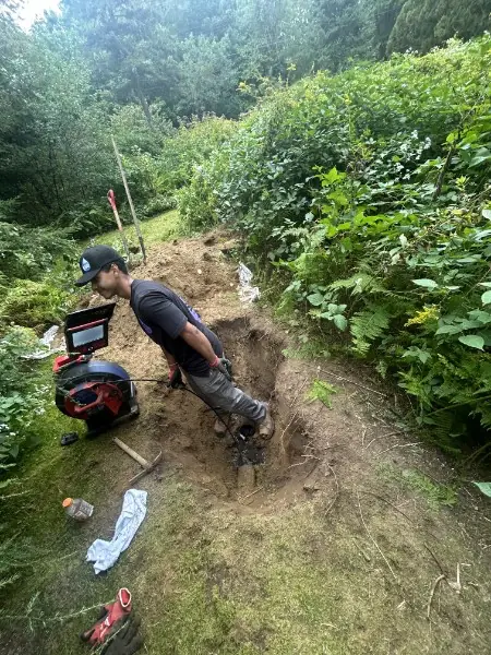 SOS technician hand-digging a trench to reach a buried line on a rural Rhode Island property